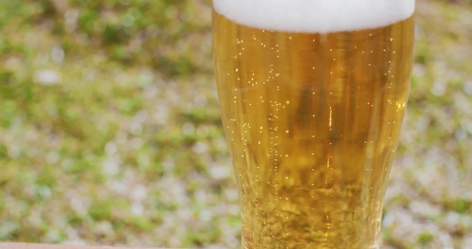 Close up on the mid section of a glass of refreshing ice cold beer or lager with a frothy top served outdoors in the garden on a summer picnic.
