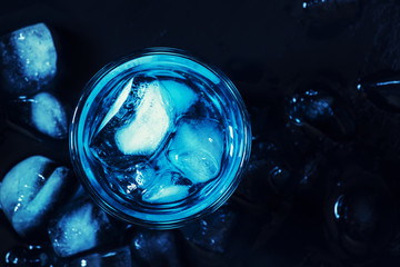Blue cocktail with ice cubes on black stone background, top view