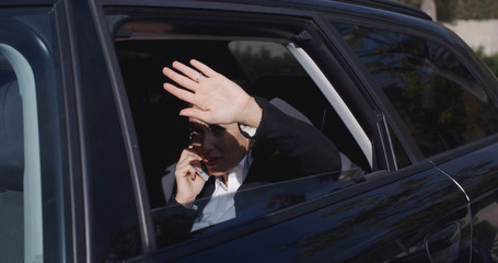 Annoyed female business woman on phone in back of car with window down trying to block the view with hand near face