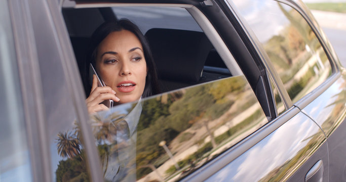 Beautiful Young Business Woman In Conversation On Phone While Sitting In Rear Seat Of Limousine Looking Out From Window