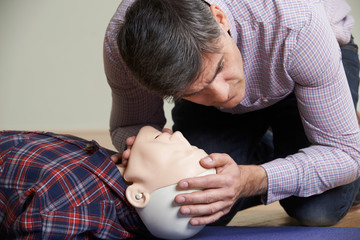 Man In First Aid Class Checking Airway On CPR Dummy