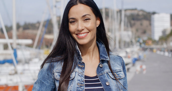 Gorgeous vivacious young woman standing outdoors at a marina looking at the camera with a lovely warm friendly smile