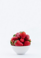 A white bowl full of strawberries on an isolated white background. Portrait orientation.