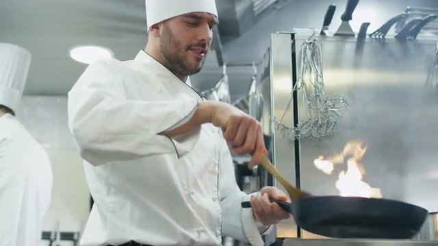 Professional chef in a commercial kitchen is preparing food in flambe style on a pan. Shot on RED Cinema Camera.
