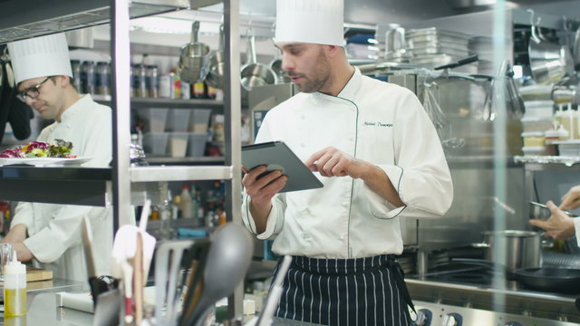 Professional chef in a commercial kitchen in a restaurant or hotel is using a tablet computer. Shot on RED Cinema Camera.