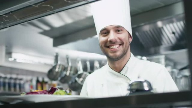 Happy professional chef in a commercial kitchen in a restaurant or hotel is serving salad. Shot on RED Cinema Camera.