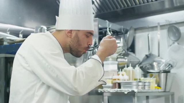 Happy professional chef in a commercial kitchen in a restaurant or hotel is tasting soup. Shot on RED Cinema Camera.