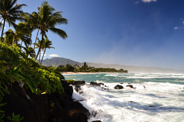 Waves crashing on rocks at Oahu's north shore coast (Turtle Beach) near the town of Haleiwa. Spray in the air; the mountain range in the background marks the western tip of Oahu, Ka'Ena Point. Hawaii.