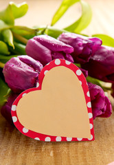 Purple tulips with heart card on wood background.