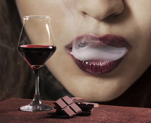 Red wine glass with chocolate and female mouth smoking