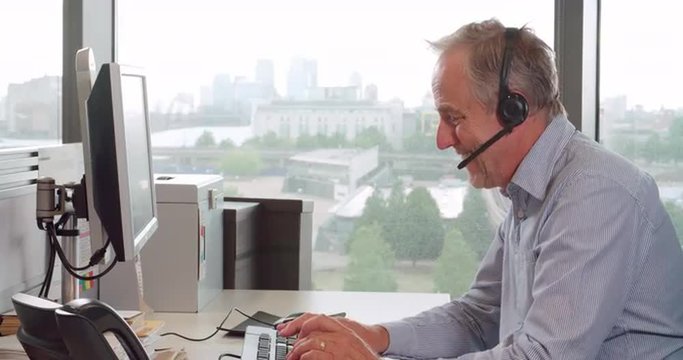 Senior male call centre worker wearing headset, side view