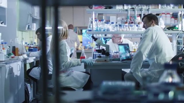 Team of caucasian scientists in white coats are working in a modern laboratory. Shot on RED Cinema Camera.