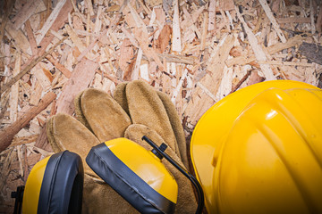 Safety leather gloves building helmet earmuffs on chipboard