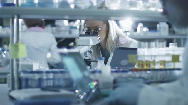 Female scientist is using a microscope and a tablet while working in a laboratory. Shot on RED Cinema Camera.