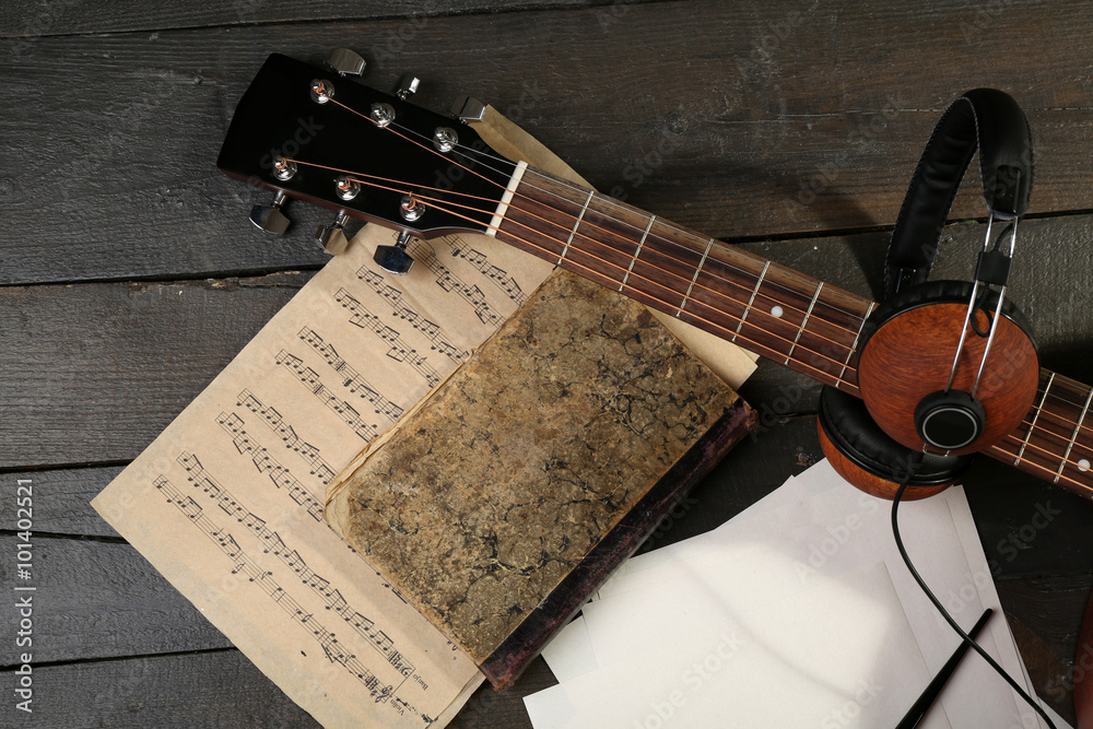 Sticker acoustic guitar, headphones, musical notes and white papers on wooden background, close up