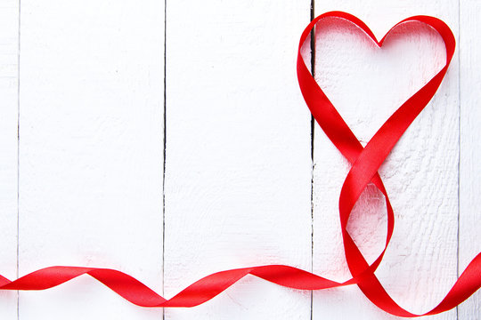 Heart shape red ribbon on white table.