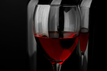 Red wine glass against bottles in a row on black background, close up