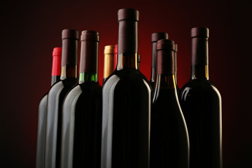 Wine bottles in a row on dark red background, close up