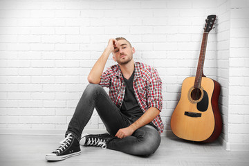 Young musician with guitar on light wall background