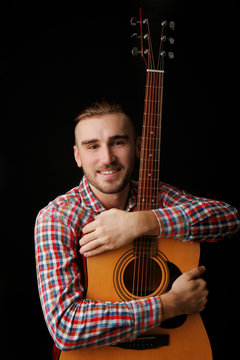 Young man with guitar on dark background