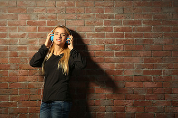Fototapeta na wymiar Young woman standing at the brick wall and listening to music