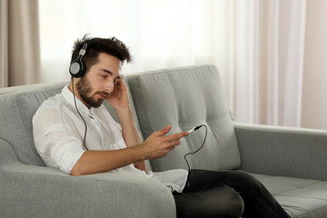 Obraz premium Young man listens music with headphones on grey sofa in the room