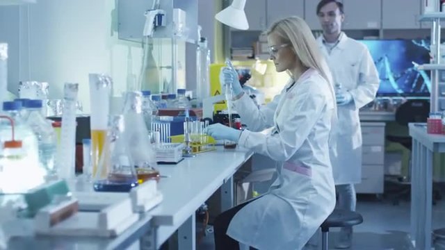  Female scientist is using a micro pipette while working in a laboratory with colleagues. Shot on RED Cinema Camera.