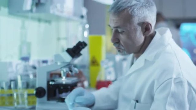 Senior scientist is working with a microscope in a laboratory with colleagues. Shot on RED Cinema Camera.