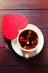 Cup of fruit tea on a limpet with red heart on wooden background closeup