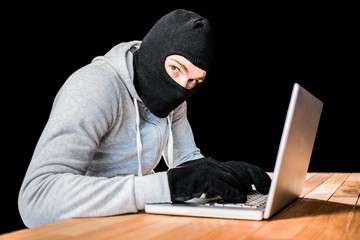 Focused thief with hood typing on laptop