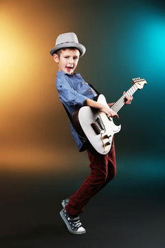 Little boy playing guitar on a dark lighted background