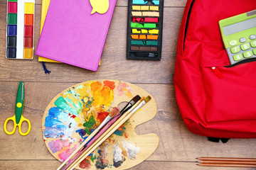 School set with backpack, palette and supplies on wooden background