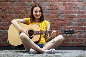 Attractive woman with tattoo playing guitar on brick background