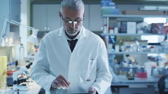 Senior scientist is walking with a tablet in a laboratory where colleagues are working.  Shot on RED Cinema Camera.