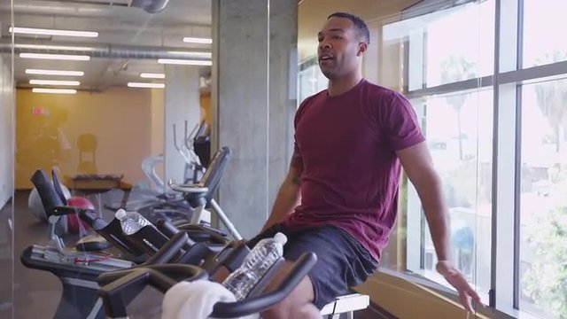Healthy fit couple Black man and Hispanic woman on stationary bikes stretching and working out in gym