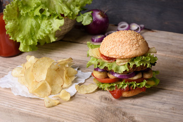 Juicy cheeseburger on wooden table with potato chips and ketchup.