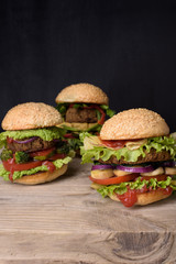 Juicy Hamburgers on sesame buns with succulent beef patties and fresh salad ingredients on a rustic wood table, dark background.