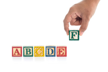 Colorful wood alphabet blocks and hand holding "F" isolated on w