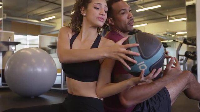 Happy fit healthy Black and Hispanic couple passing medicine ball back and forth in gym working out