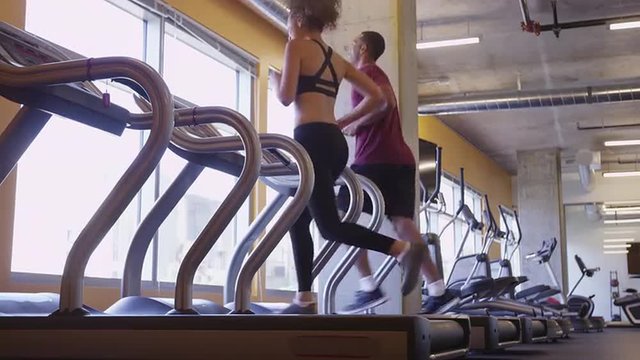 Hispanic and Black couple running together on treadmills in a gym