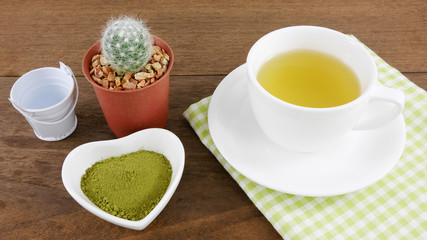 The Japanese matcha green tea powder on ceramic heart shaped bowl and cup of hot green tea with cotton fabric on wooden planks.