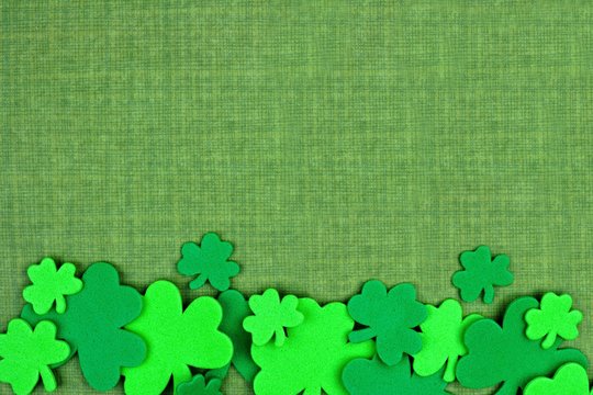 St Patricks Day bottom border of shamrock confetti over a green linen background