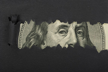Benjamin Franklin macro peeking through torn black paper - obrazy, fototapety, plakaty