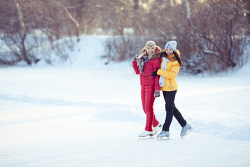 Fototapeta na wymiar two beautiful girls ice skating outdoor on a warm winter day.