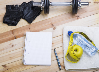 Sport Equipment. Dumbbells,  Gloves, Towel, Apple, Tape Measure, Bottle Of Water And Notebook To Workout Plan On Wooden Table. Sport Fitness Background