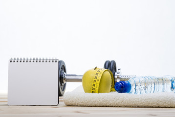 Sport Equipment. Dumbbells,  Towel, Apple, Tape Measure, Bottle Of Water And Notebook To Workout Plan On Wooden Table With White Background. 