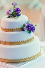 Fototapeta na wymiar The white wedding cake, decorated with the soil gold and violet floral. Selective focus.