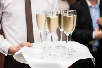 Restaurant waiter brings people and alcohol champagne on a tray