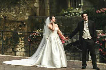 Happy romantic married couple holding hands on stone bridge with