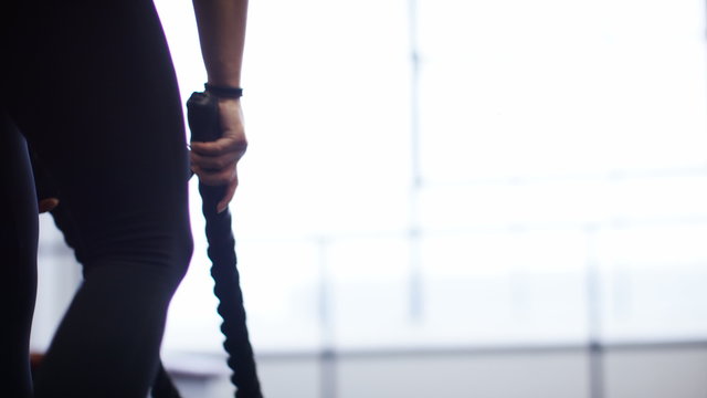 Hands of an unseen woman picking up battle ropes and exercising in the gym, in slow motion